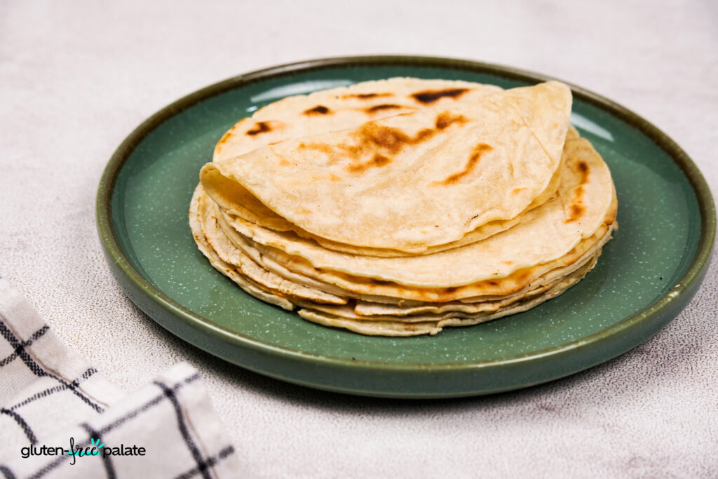 Wide angle view of a full stack of gluten-free tortillas placed on a green ceramic plate, with a soft napkin.