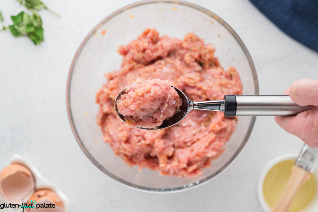 A cookie scoop portioning the meatball mixture.