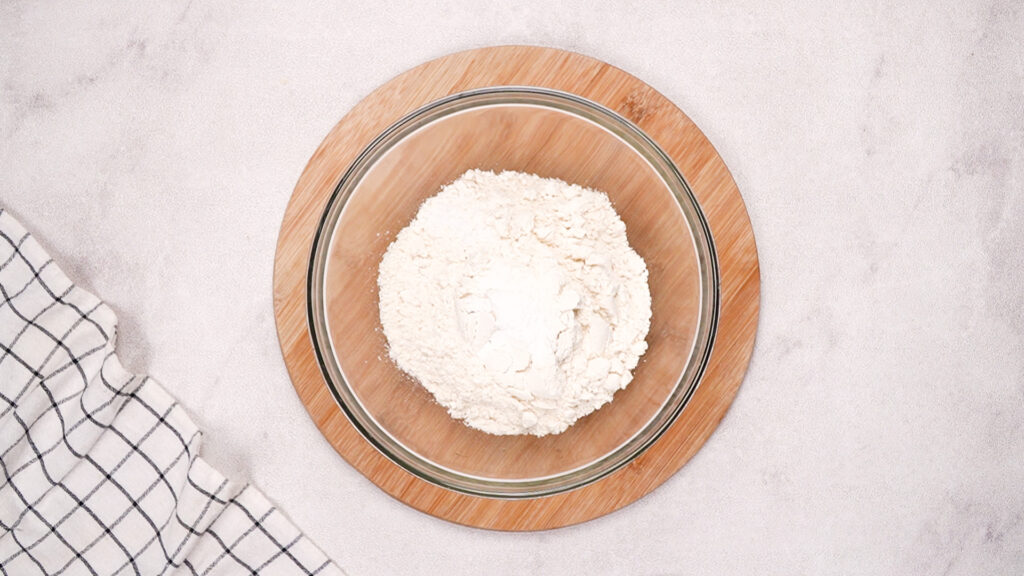 A glass bowl filled with masa harina sitting on a wooden board, ready to be mixed for gluten-free taco shells.