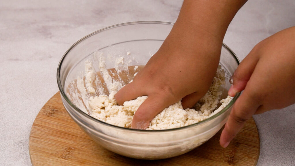 Hands mixing the dough in a glass bowl, combining all ingredients into a uniform dough.