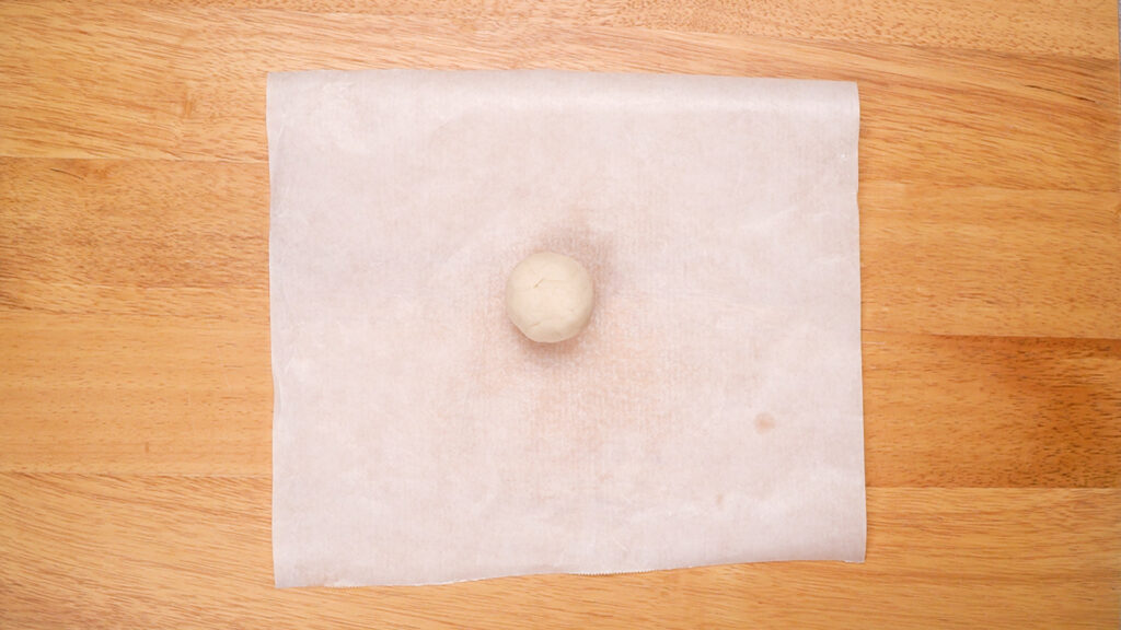 A single dough ball placed on a sheet of parchment paper, ready to be rolled out.