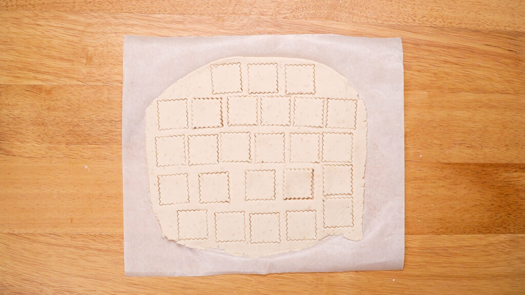 The rolled-out dough with neatly cut square cracker shapes, showing the uniformity of size and thickness for even baking.