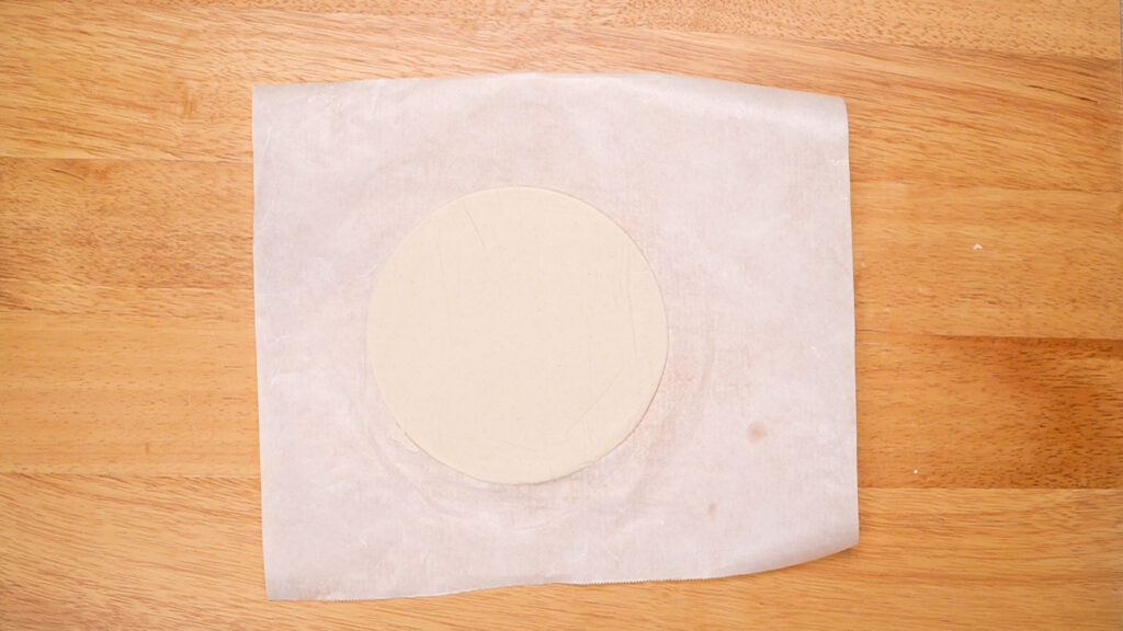 The dough ball rolled into a thin, round tortilla shape between two sheets of parchment paper.