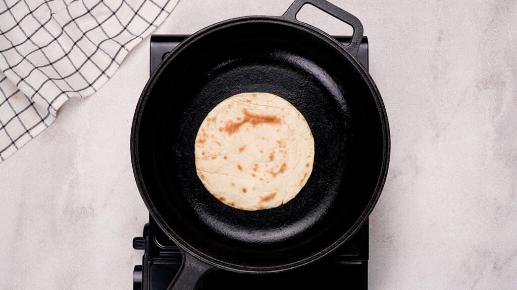 A taco shell with golden brown spots, flipped and cooked on the second side in the skillet.