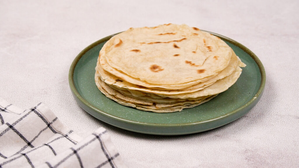 A stack of finished gluten-free taco shells neatly arranged on a green plate, ready to serve or store.