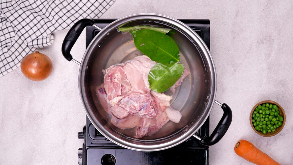 Raw chicken and bay leaves in a pot of water on the stove.