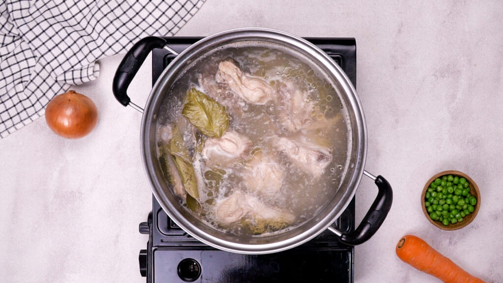 Chicken simmering in water with bay leaves in the same pot.