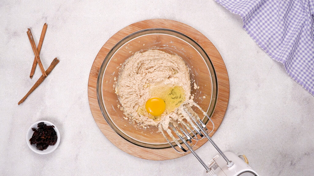 The mixture has been creamed, and a cracked egg is added on top, with beaters in the bowl.