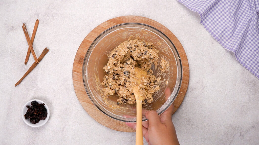 The final cookie dough is thick and chunky, being stirred with a wooden spoon.