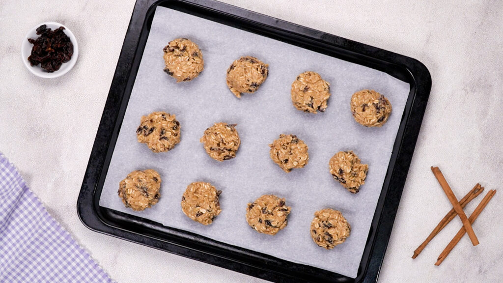 Scoops of dough are placed on a parchment-lined baking sheet, spaced apart.