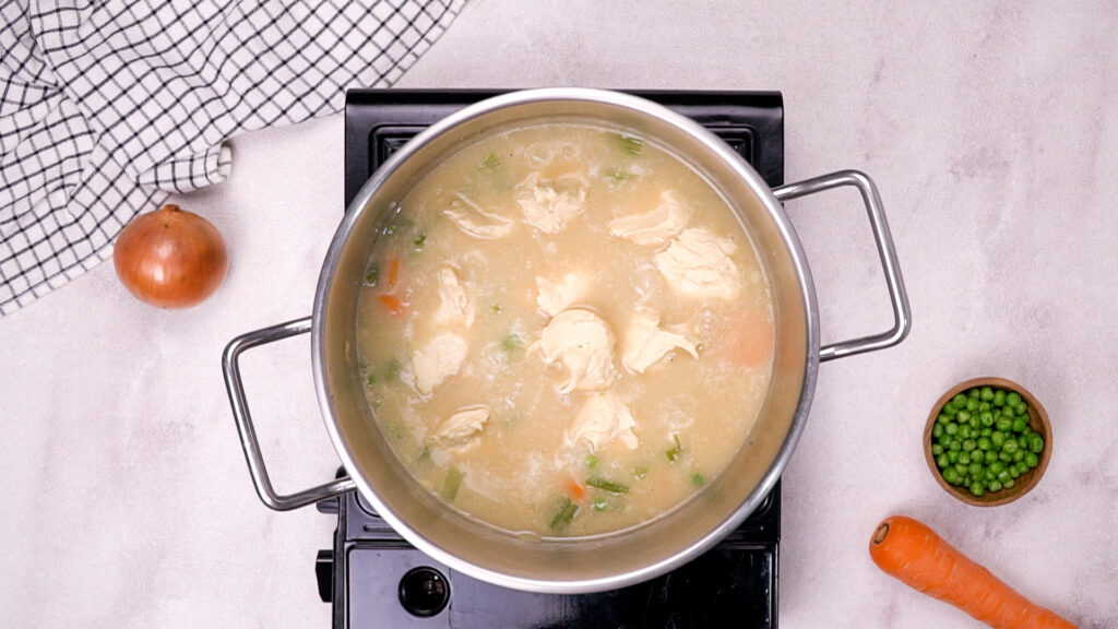 Dumplings cooking in the soup pot with broth and vegetables.