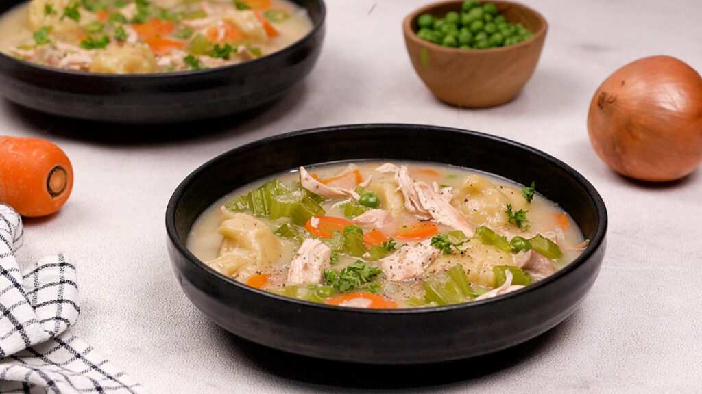 Cooked gluten-free chicken and dumpling soup served in a black bowl.
