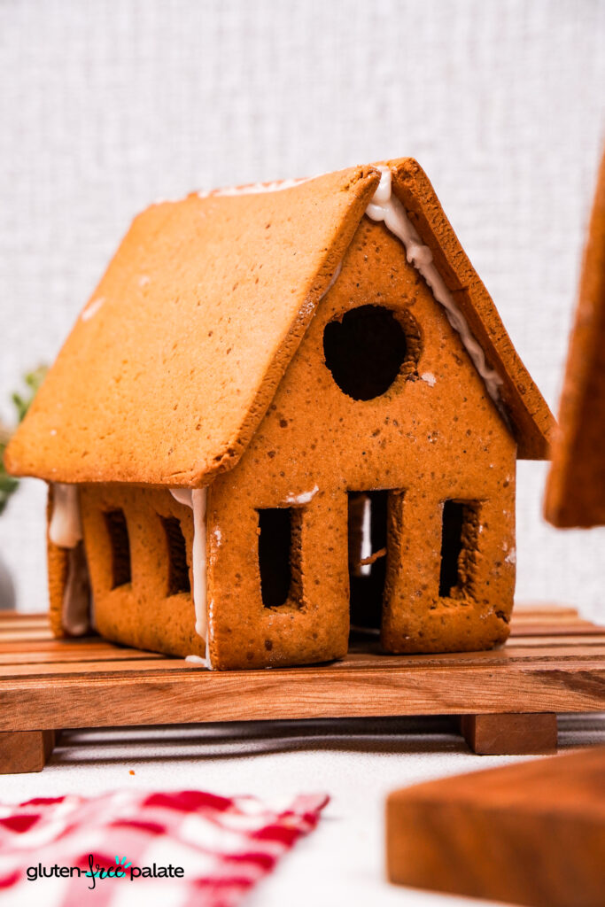 Close-up of the front side of a gluten-free gingerbread house with detailed windows and a round upper window, highlighting the gingerbread texture and icing.