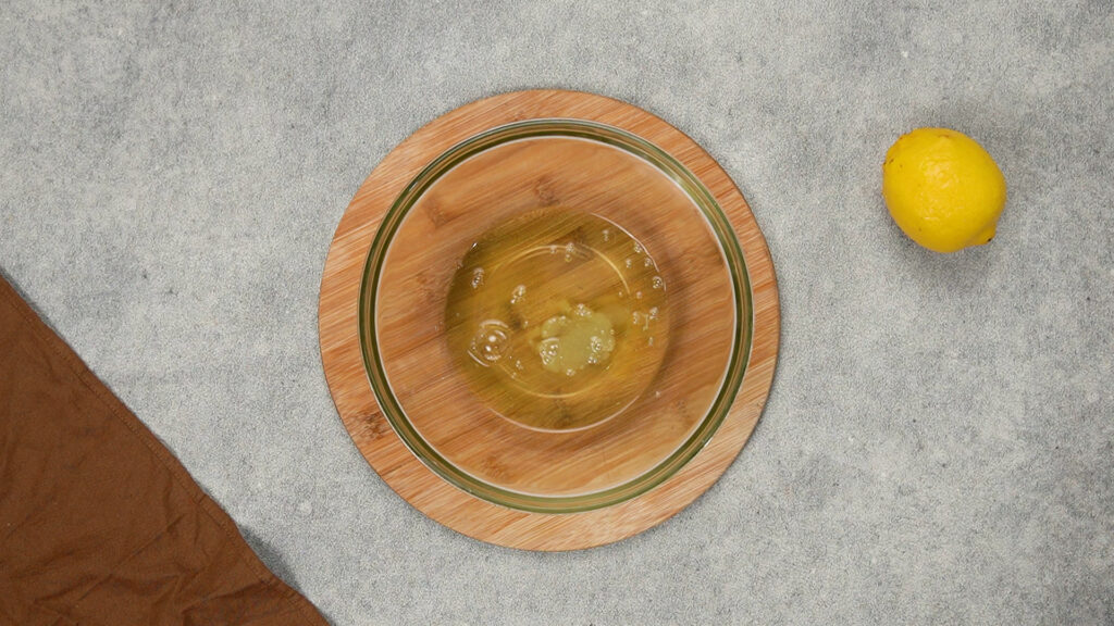 Large glass bowl with raw egg whites and lemon juice on a wooden board, the first step in making gluten-free cloud bread.