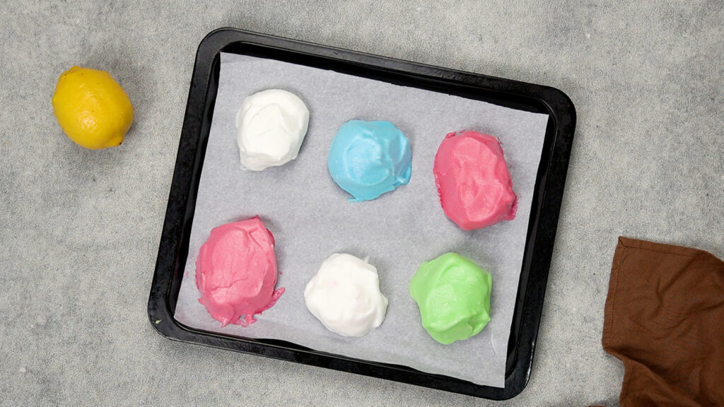 Six scoops of pastel-colored gluten-free cloud bread batter shaped into domes on parchment-lined baking tray.