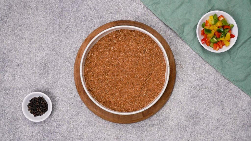 Around white dish heaped with orange-brown homemade fajita seasoning blend, placed on a wooden board.