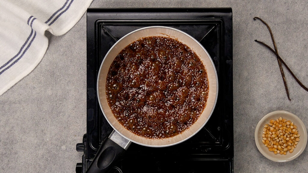 The caramel mixture in the saucepan has come to a rolling, amber-colored boil, with small bubbles rising across the surface.
