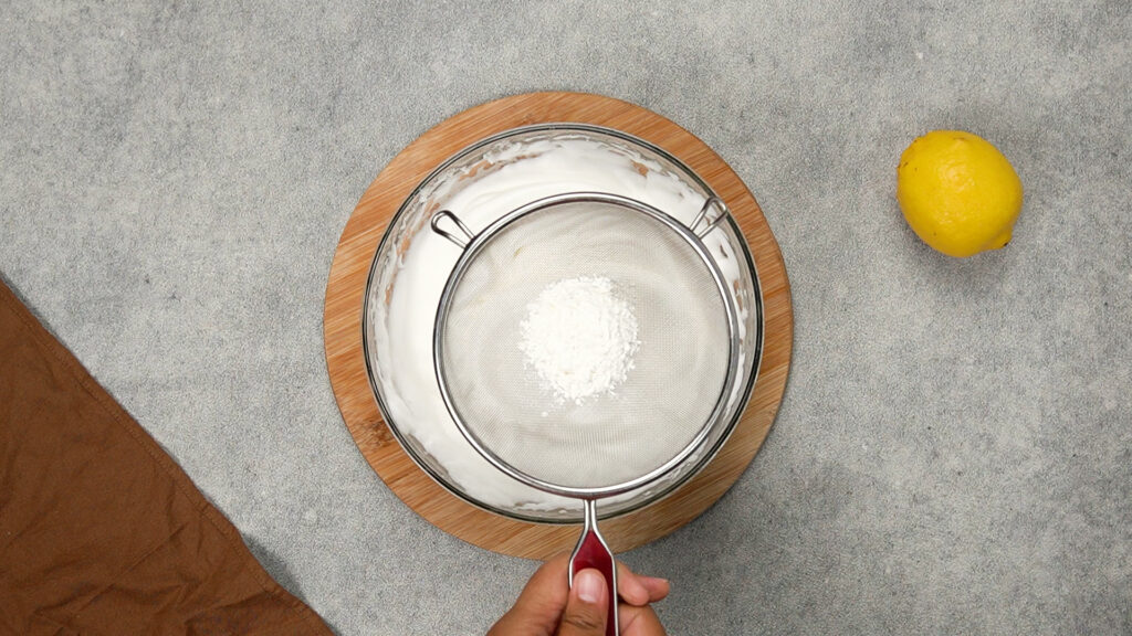 Cornstarch being sifted over a fluffy bowl of whipped egg whites to create structure in gluten-free cloud bread batter.