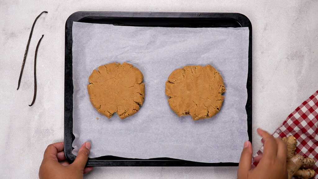 Two portions of gingerbread dough flattened into disks on parchment paper, ready for chilling.