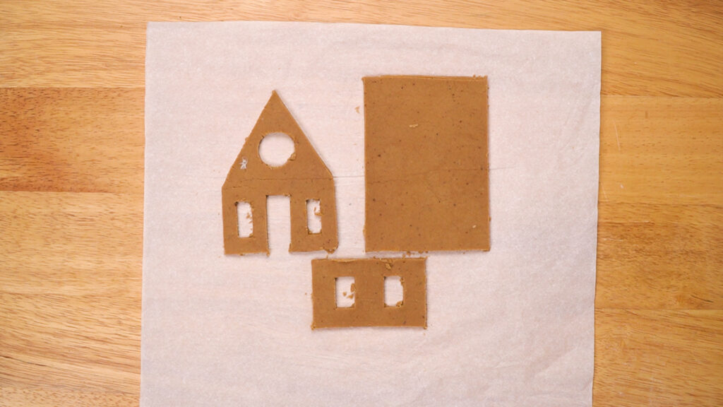 Rolled out gingerbread dough cut into house shapes for assembling a gingerbread house.