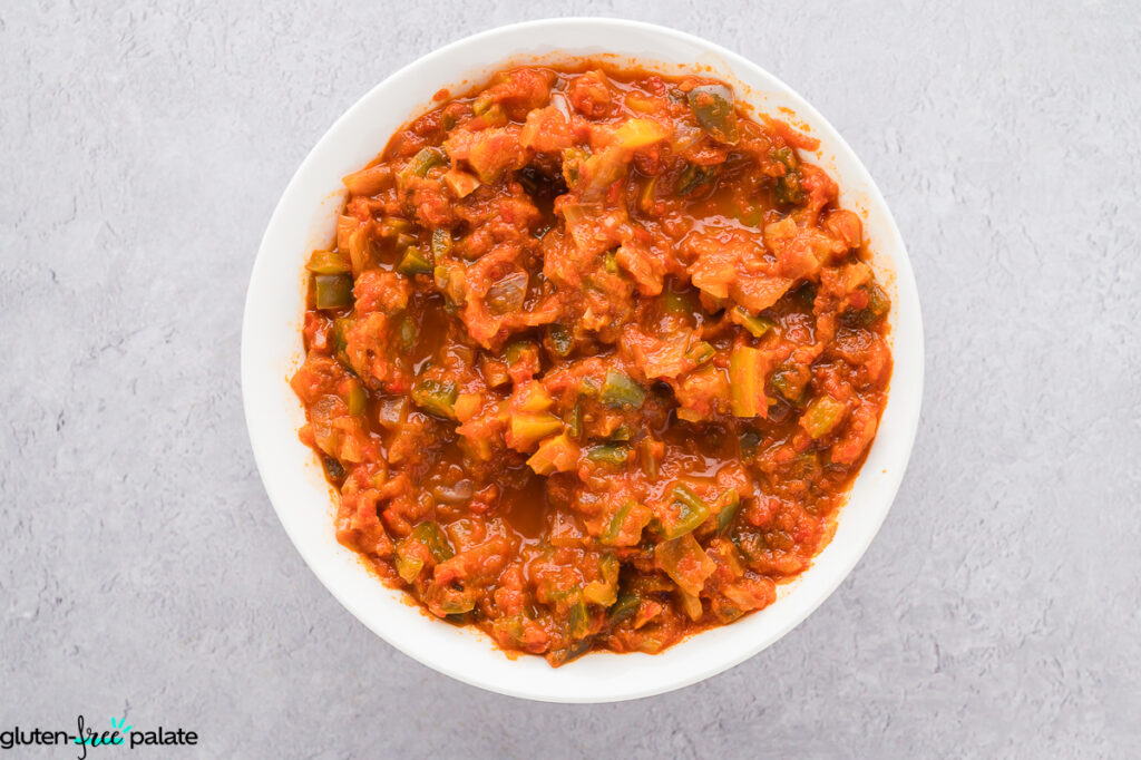 Fully cooked gluten-free bell pepper salsa served in a white bowl, showing softened chunks of onion and pepper.