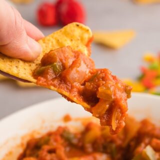 Hand holding a tortilla chip scooped with chunky bell pepper salsa, showing texture and diced vegetables.