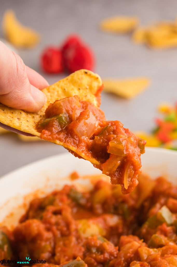Hand holding a tortilla chip scooped with chunky bell pepper salsa, showing texture and diced vegetables.