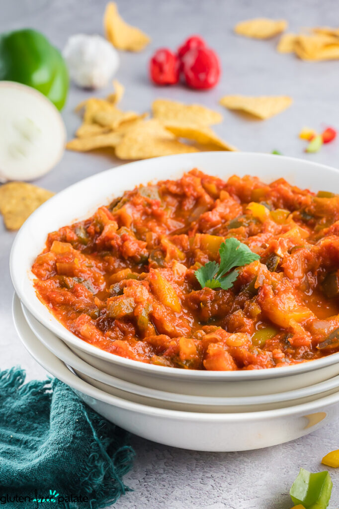 Side angle of cooked gluten-free salsa garnished with a cilantro leaf, with chips and bell peppers in the background.