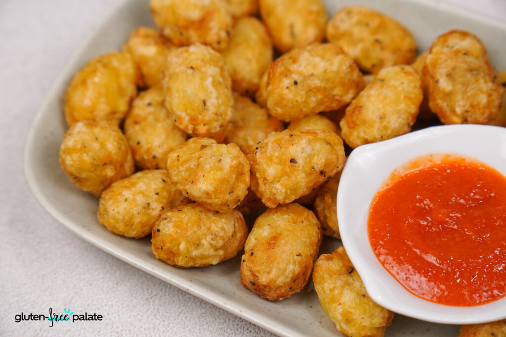 Golden crispy gluten-free tater tots served on a platter with a ketchup.