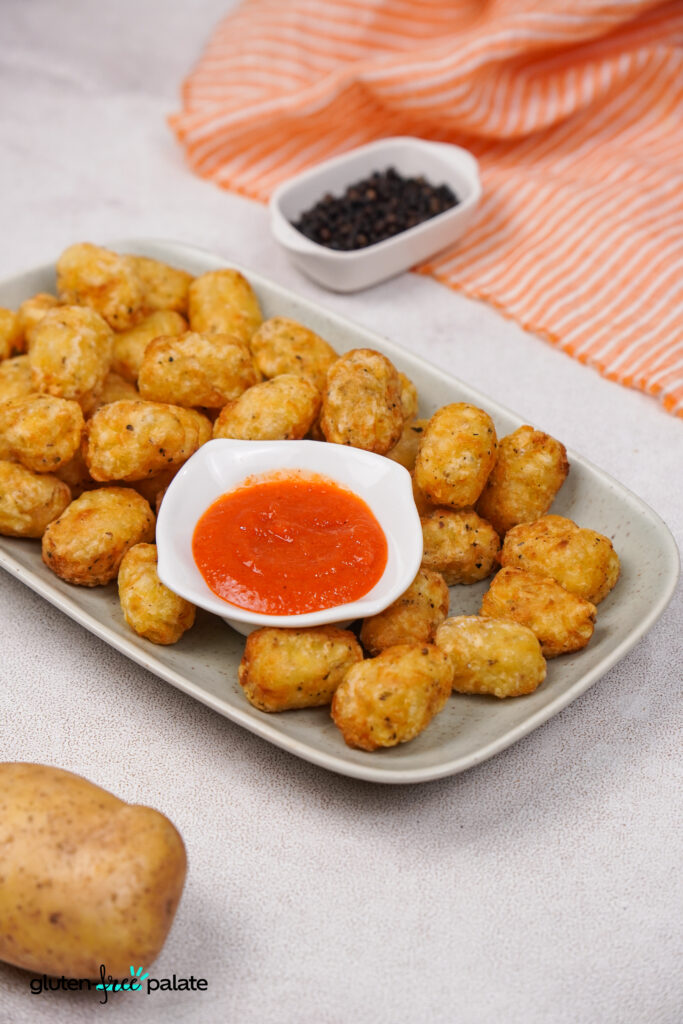 Golden crispy gluten-free tater tots served on a platter with a ketchup.