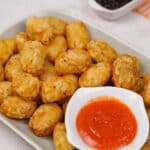 Golden crispy gluten-free tater tots served on a platter with a ketchup.