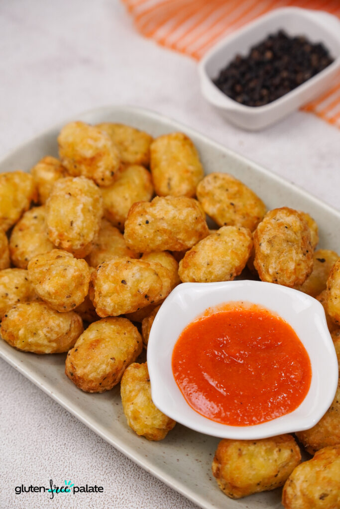 Golden crispy gluten-free tater tots served on a platter with a ketchup.