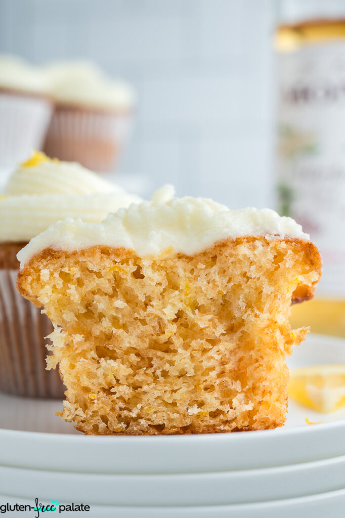 Close-up side view of a moist, fluffy gluten-free lemon elderflower cupcake cut in half, topped with creamy frosting and lemon zest.