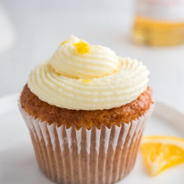 Side view of a gluten-free lemon elderflower cupcake with piped frosting and lemon zest garnish, placed on a white plate.