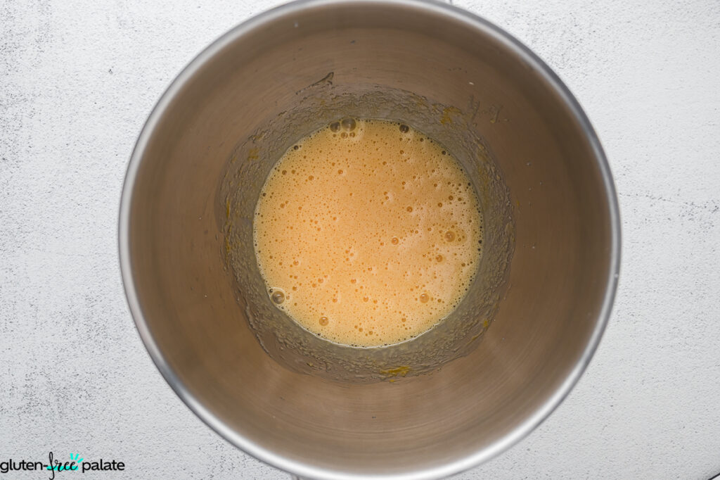 Egg, sugar and oil mixture whisked together in a stainless-steel mixing bowl, showing a frothy consistency.