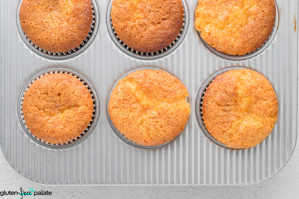 Freshly baked golden gluten-free lemon elderflower cupcakes cooling in a silver cupcake baking tray.