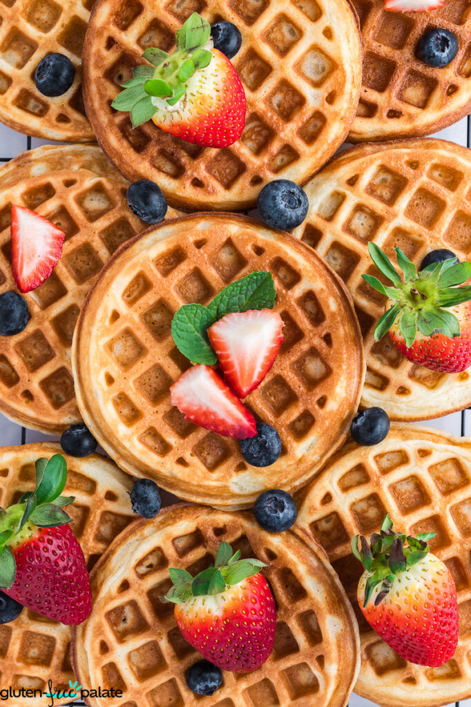 Golden mochi waffles topped with strawberries, blueberries, and mint leaves on a cooling rack.