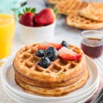 A stack of mochi waffles with berries, a dusting of powdered sugar and syrup.