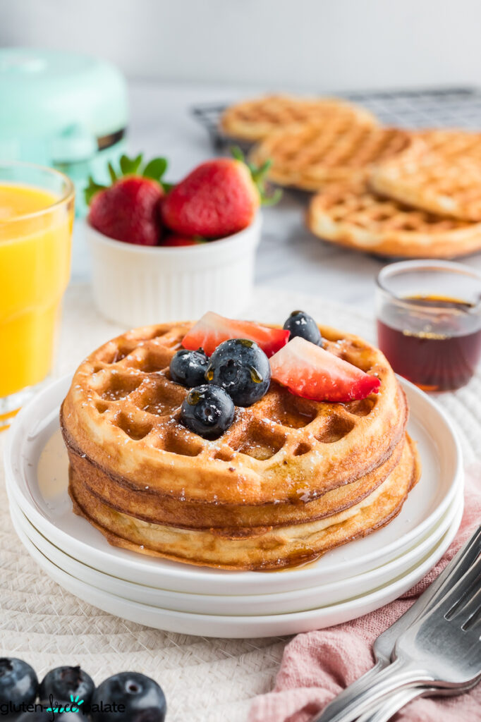 A stack of mochi waffles with berries, a dusting of powdered sugar and syrup.