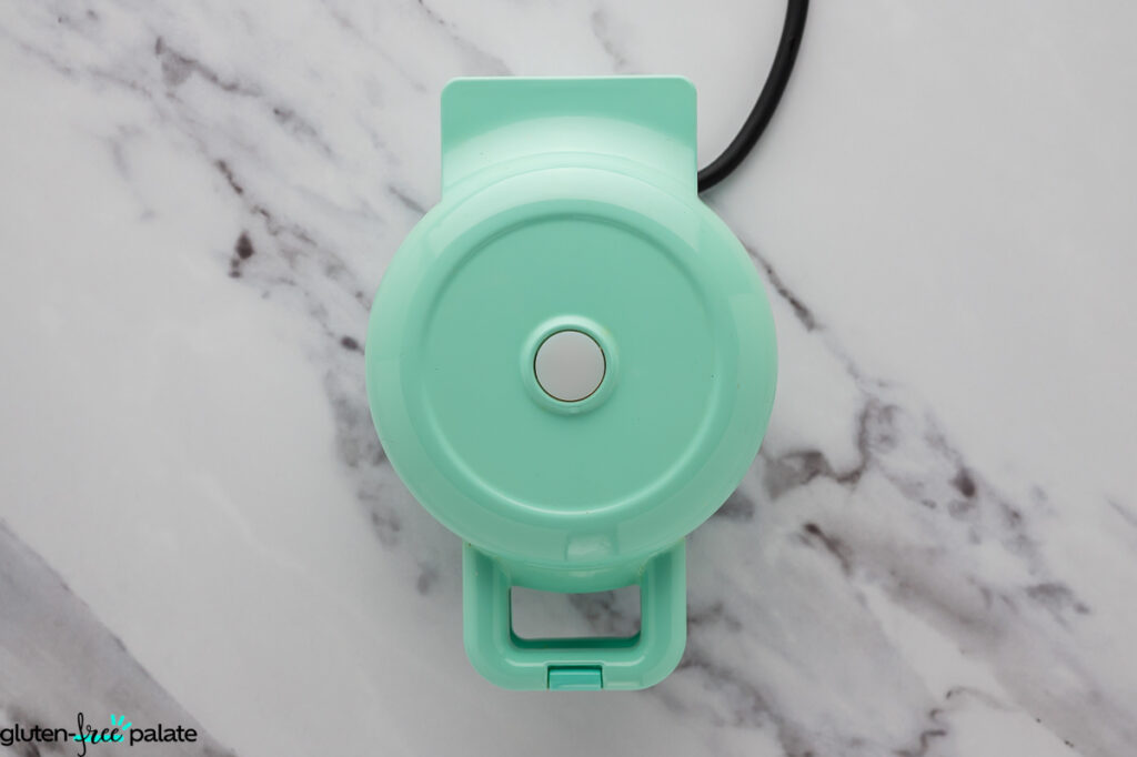 Closed mini waffle maker preheating on a marble countertop.