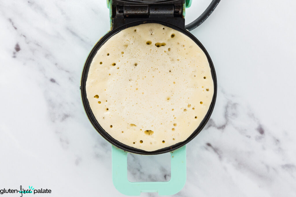 Mini waffle maker filled with mochi waffle batter ready to cook.