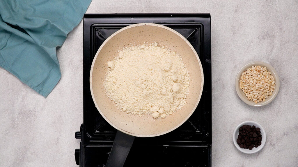 Overhead view of a frying pan on a stovetop containing almond flour.