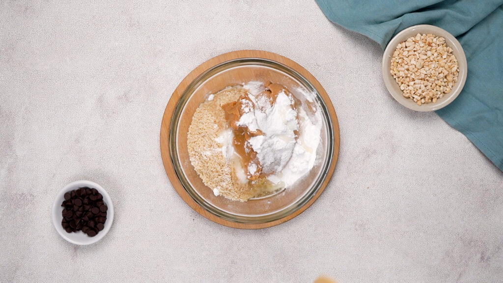 Mixing bowl with crushed crumbs, peanut butter, powdered sugar, and other ingredients ready to be combined.