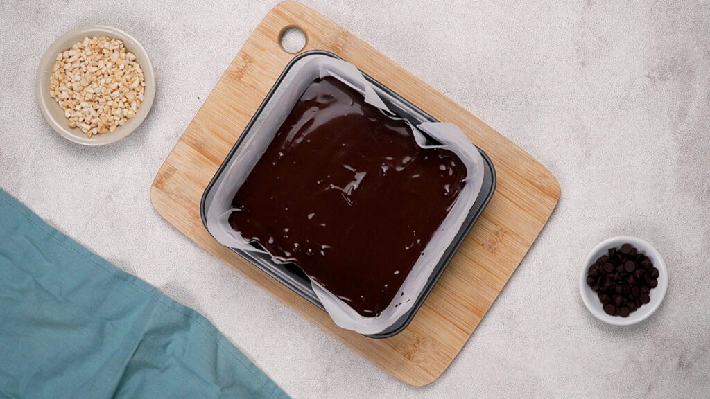 Baking tin with peanut butter layer now topped with a smooth, glossy layer of melted chocolate.