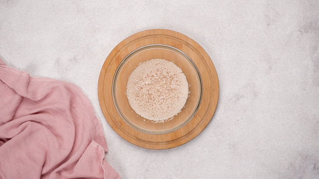 glass bowl with foamy yeast mixture sitting on a wooden board.