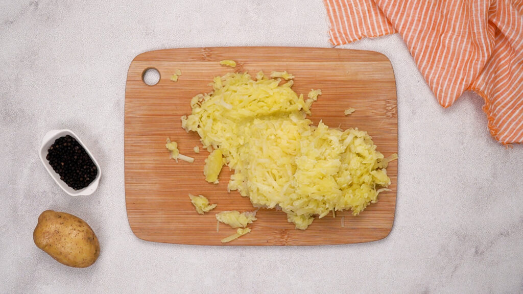 Freshly grated boiled potatoes on a wooden cutting board.