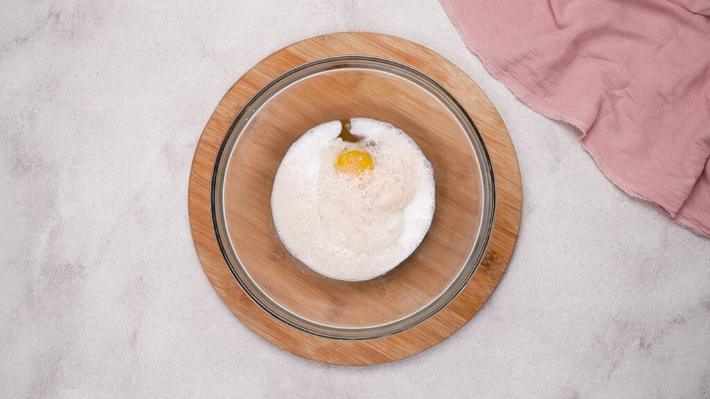 A mixing bowl with coconut milk, yeast mixture, and an egg before whisking together.