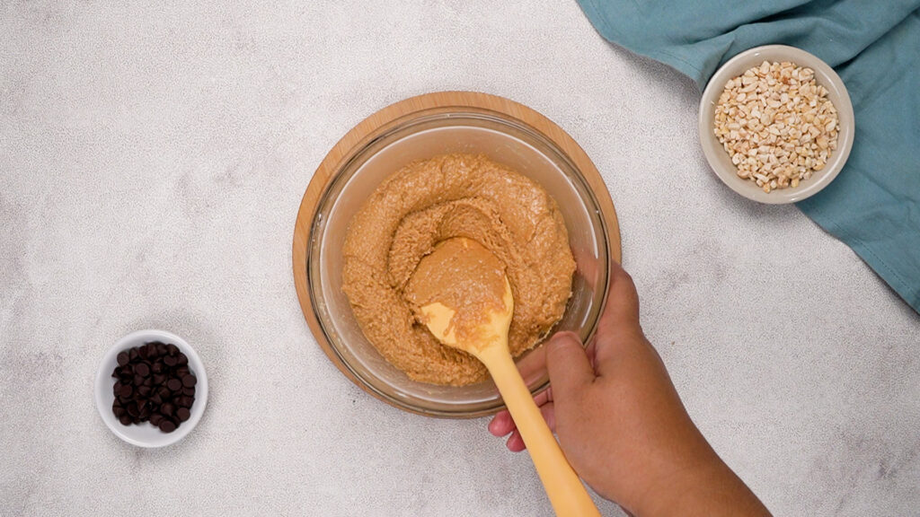 Close-up of a mixing bowl with peanut butter mixture being stirred using a yellow spatula