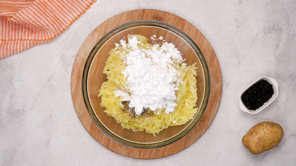 Grated potatoes mixed with potato starch and seasonings in a bowl.