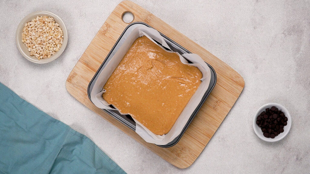 Square baking tin lined with parchment paper filled with smooth peanut butter mixture.